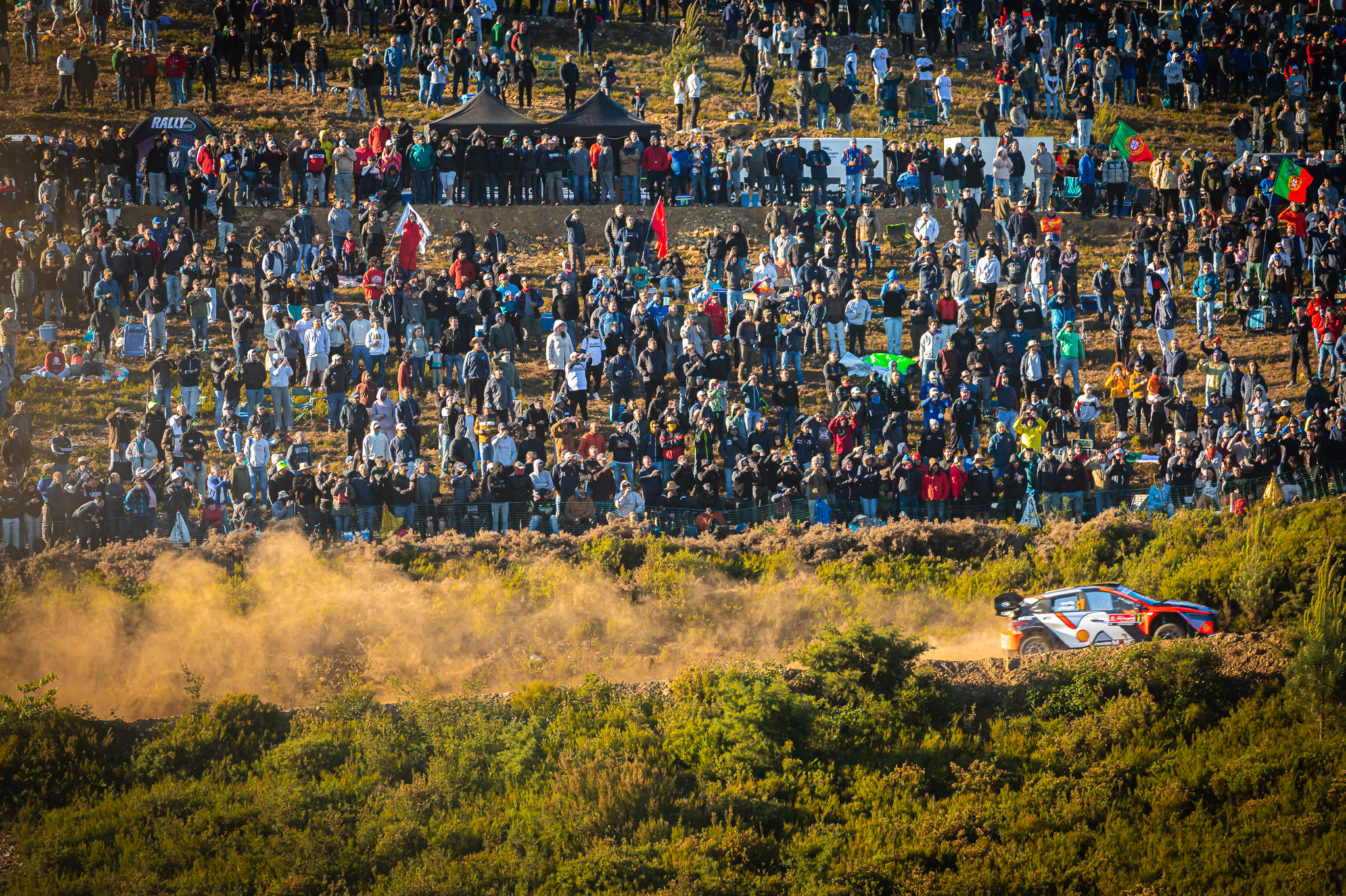 Multidão observa carro de rally em paisagem ampla